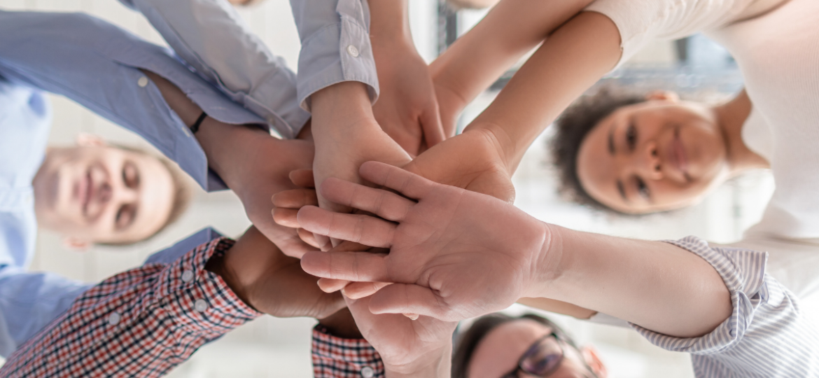 Workplace Culture Blog Graphic that showcases a a group of people putting their hands together for a team huddle.