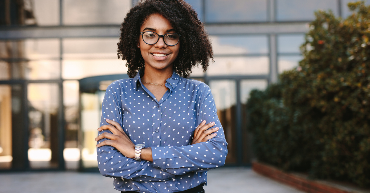 Retaining Talent Graphic: Photo of a young woman in a blue button up. Her arms are crossed and she is standing confidently in front of a glass building. She's smiling.